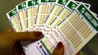 Pessoa segura em suas mãos cartões de apostas da Mega Sena