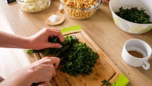 Em imagem ilustrativa, pessoa corta hortaliça vede em uma tábua de maneira