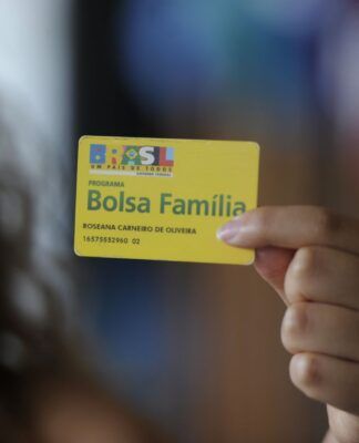 Em imagem ilustrativa, jovem segura o cartão do Bolsa Família