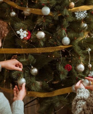 Casal colocando enfeites cinzas em uma grande árvore de Natal verde