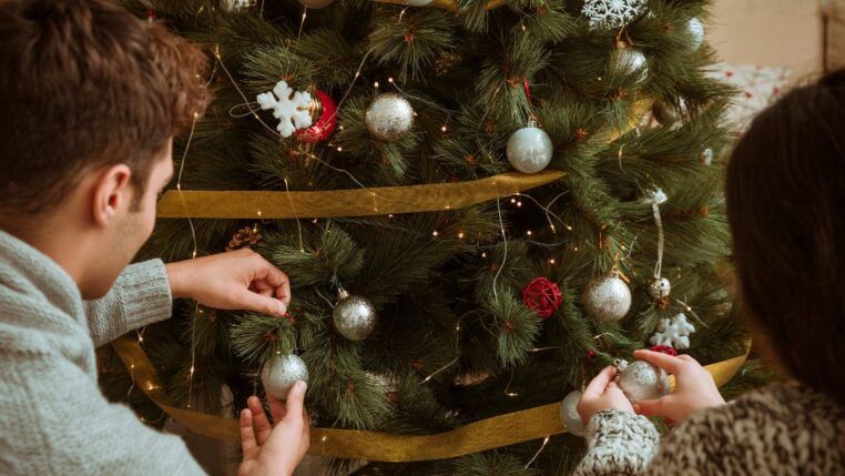 Casal colocando enfeites cinzas em uma grande árvore de Natal verde
