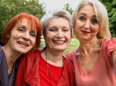 Três mulheres maduras sorrindo juntas em uma selfie ao ar livre.