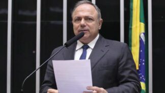 A foto é um retrato em plano médio-fechado de Eduardo Pazuello, ex-Ministro da Saúde e atualmente deputado federal, no plenário da Câmara dos Deputados.