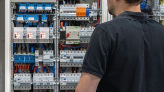 Em imagem ilustrativa, homem olha fixamente para painel elétrico.