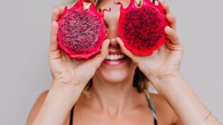 Em imagem ilustrativa, mulher segura uma Pitaya partida ao meio ,acima dos seus olhos.