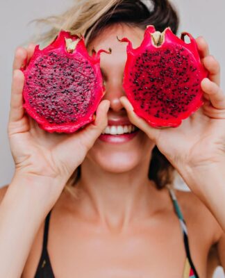 Em imagem ilustrativa, mulher segura uma Pitaya partida ao meio ,acima dos seus olhos.