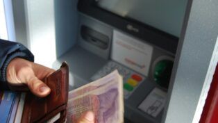 Em imagem ilustrativa, pessoa saca dinheiro em banco.