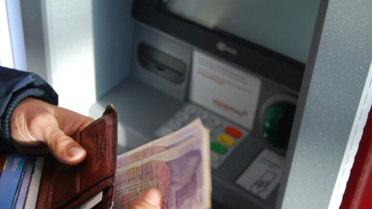 Em imagem ilustrativa, pessoa saca dinheiro em banco.