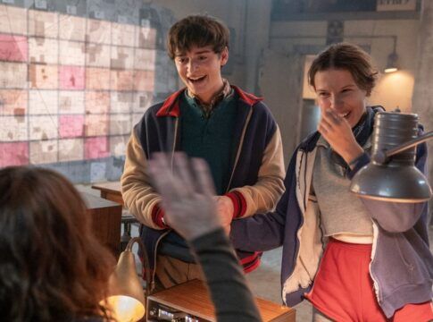 Esta é uma imagem colorida, em ambiente interno, que captura um momento de aparente alegria e intensa atividade de investigação, tipicamente associado à série Stranger Things.