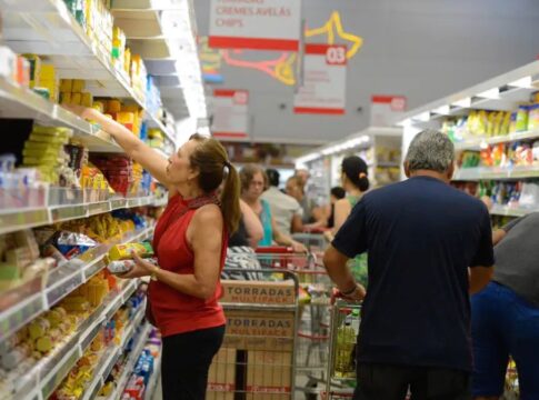 mulher pega produto em prateleira de supermercado