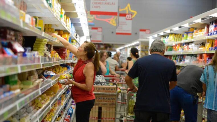 mulher pega produto em prateleira de supermercado