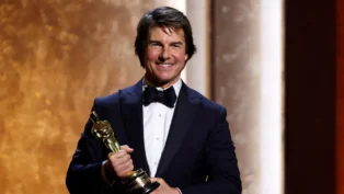 Ator Tom Cruise veste smoking e sorri com um Oscar honorário nas mãos, em evento especial da Academia