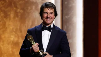 Ator Tom Cruise veste smoking e sorri com um Oscar honorário nas mãos, em evento especial da Academia