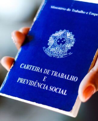 Em imagem ilustrativa, pessoa segura em suas mãos, uma carteira de trabalho brasileira.