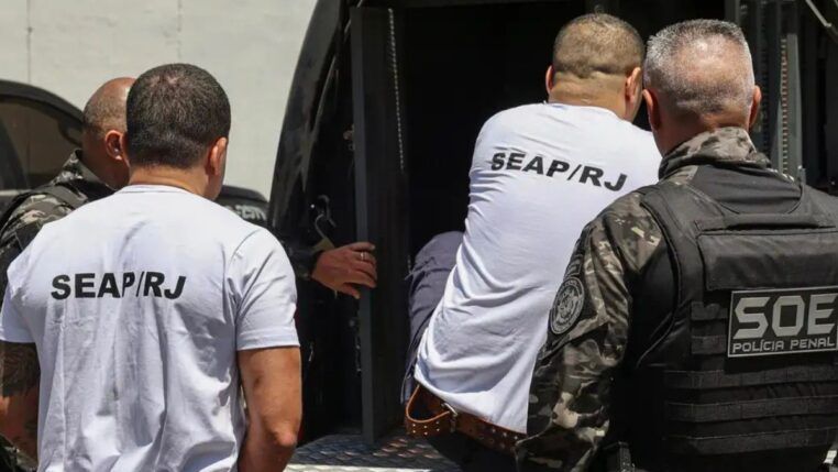 homens entrando em veículo policial para serem transferidos