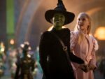 As personagens Elphaba e Glinda olham juntos de mãos dadas para algo que deixa eles felizes