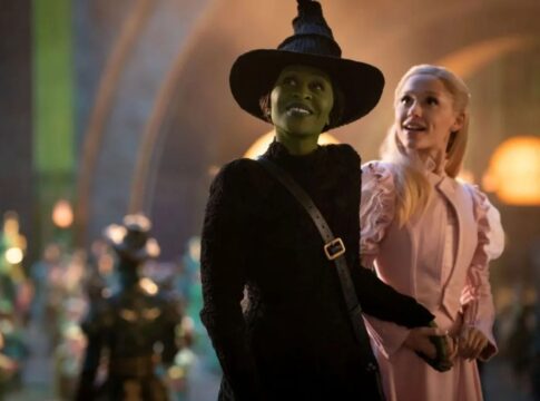 As personagens Elphaba e Glinda olham juntos de mãos dadas para algo que deixa eles felizes