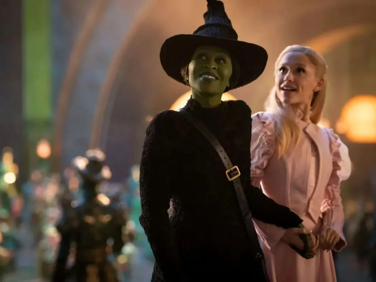 As personagens Elphaba e Glinda olham juntos de mãos dadas para algo que deixa eles felizes