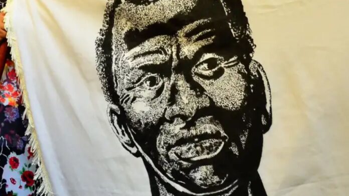 A imagem é um retrato artístico em preto e branco de Zumbi dos Palmares, estampado em um grande tecido ou bandeira de cor creme/branca. O rosto de Zumbi ocupa o centro da imagem. O estilo do desenho é de alto contraste (parecido com xilogravura ou serigrafia), usando densas áreas de preto e branco para criar textura e sombreamento.