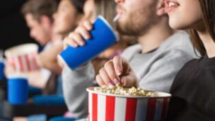Em imagem ilustrativa, pessoas assistem ao cinema com pipoca