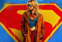 Foto promocional do filme Supergirl onde a atriz Milly Alcock (mulher loira, de óculos escuros e casaco preto por cima do uniforme de super-heroi) aparece olhando para o lado