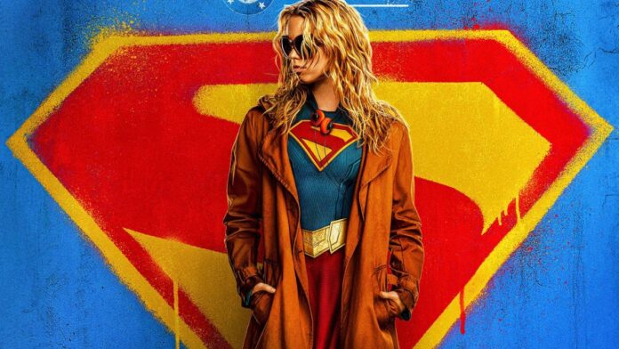 Foto promocional do filme Supergirl onde a atriz Milly Alcock (mulher loira, de óculos escuros e casaco preto por cima do uniforme de super-heroi) aparece olhando para o lado