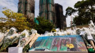 Flores e um quadro homenageiam as vítimas do incêndio, com os prédios ao fundo