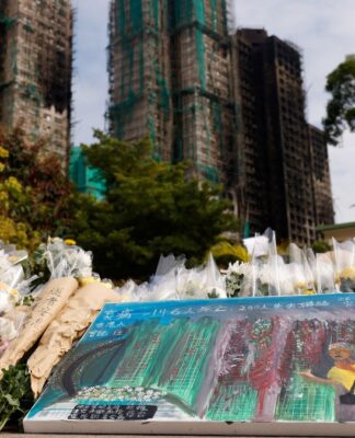 Flores e um quadro homenageiam as vítimas do incêndio, com os prédios ao fundo