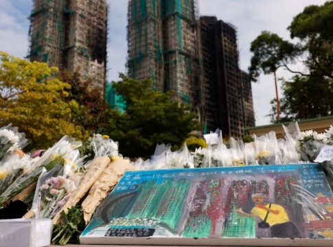 Flores e um quadro homenageiam as vítimas do incêndio, com os prédios ao fundo