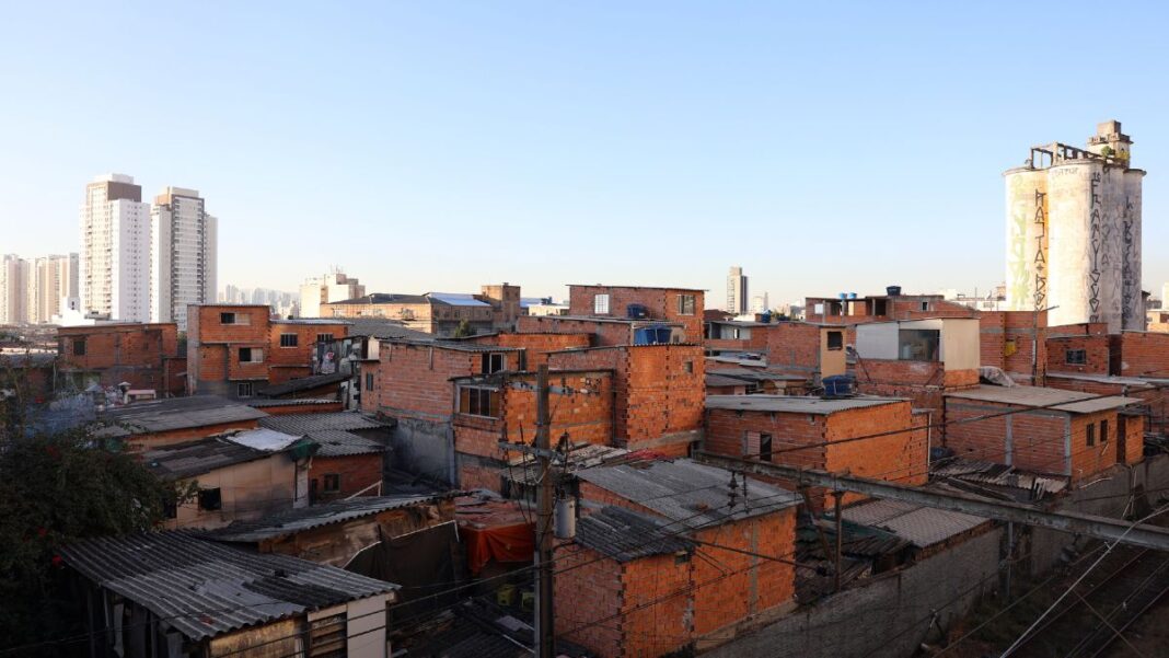 Imagem de favela no primeiro plano, com prédios de classe média ao fundo