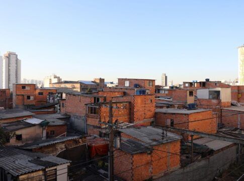 Imagem de favela no primeiro plano, com prédios de classe média ao fundo