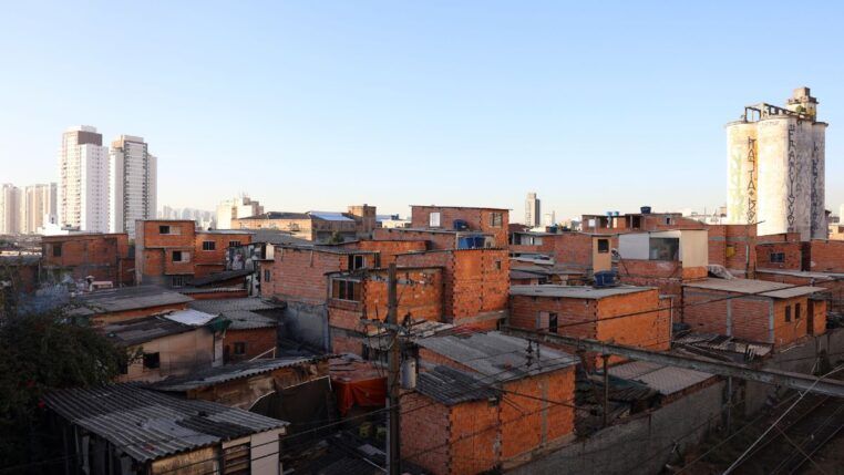 Imagem de favela no primeiro plano, com prédios de classe média ao fundo