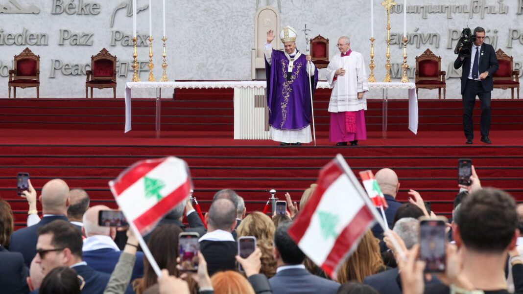 Papa Leão 14 acena aos fiéis durante missa; fiéis agitam bandeiras do Líbano