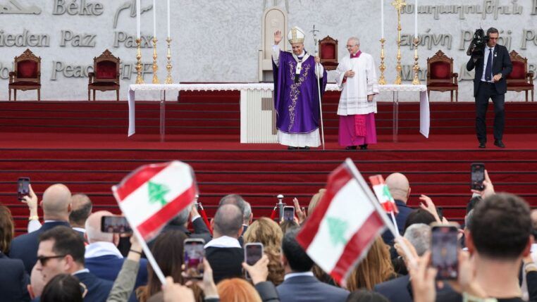 Papa Leão 14 acena aos fiéis durante missa; fiéis agitam bandeiras do Líbano
