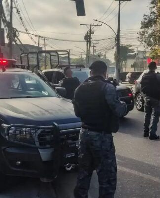 Policiais militares, de costas, carregam armas ao lado de camburões