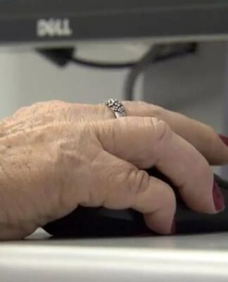 Uma mão de uma mulher idosa mexe no mouse diante de um computador