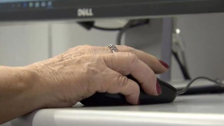 Uma mão de uma mulher idosa mexe no mouse diante de um computador