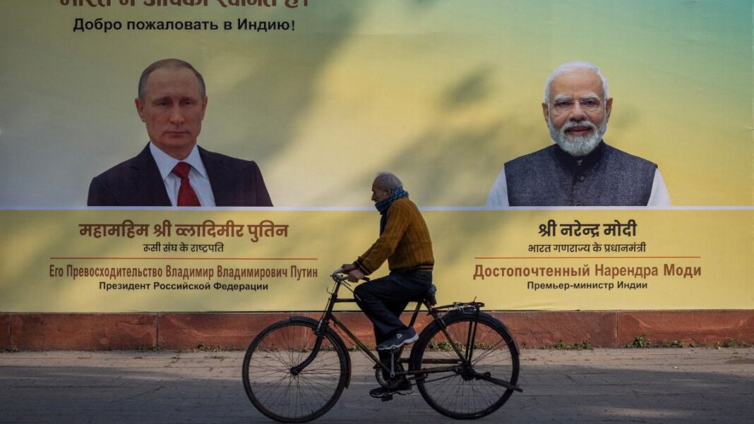 Indiano anda de bicicleta na rua à frente de um outdoor com as imagens de Putin e do primeiro-ministro indiano