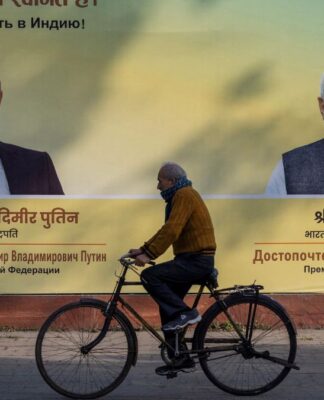 Indiano anda de bicicleta na rua à frente de um outdoor com as imagens de Putin e do primeiro-ministro indiano