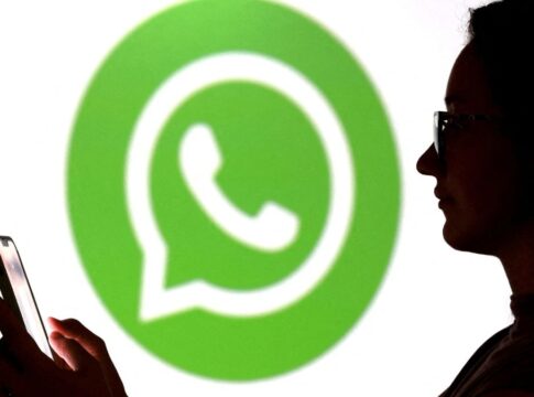 Pessoa olha para seu celular enquanto aparece o logo do Whatsapp ao fundo