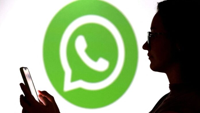 Pessoa olha para seu celular enquanto aparece o logo do Whatsapp ao fundo