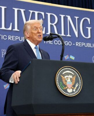 Donald Trump fala ao microfone à frente de painel onde está escrita a mensagem 