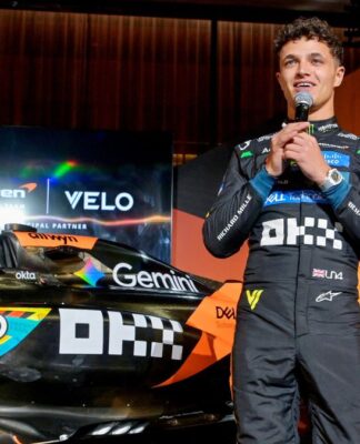 Lando Norris fala ao microfone ao lado da sua McLaren e do companheiro Oscar Piastri em evento pré-GP