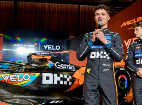 Lando Norris fala ao microfone ao lado da sua McLaren e do companheiro Oscar Piastri em evento pré-GP