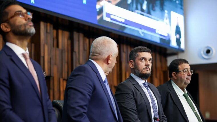 Presidente da Alerj, Rodrigo Bacellar olha para cima ao lado de outros deputados na mesa da assembleia