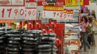 Imagem dentro de um mercado, mostrando várias placas de preços e alimentos nas prateleiras