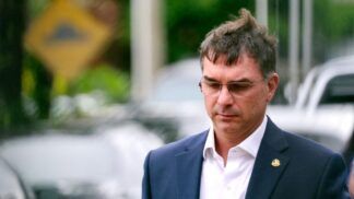 Flávio Bolsonaro, de paletó e óculos de grau, após conceder entrevista na rua