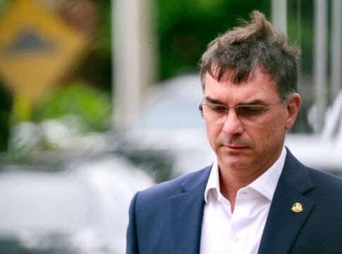 Flávio Bolsonaro, de paletó e óculos de grau, após conceder entrevista na rua