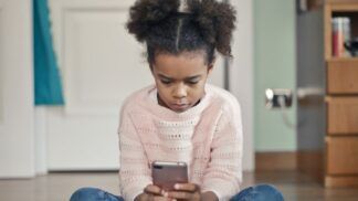 Criança de blusa rosa e calça jeans concentrada enquanto mexe no celular