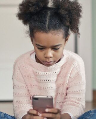 Criança de blusa rosa e calça jeans concentrada enquanto mexe no celular